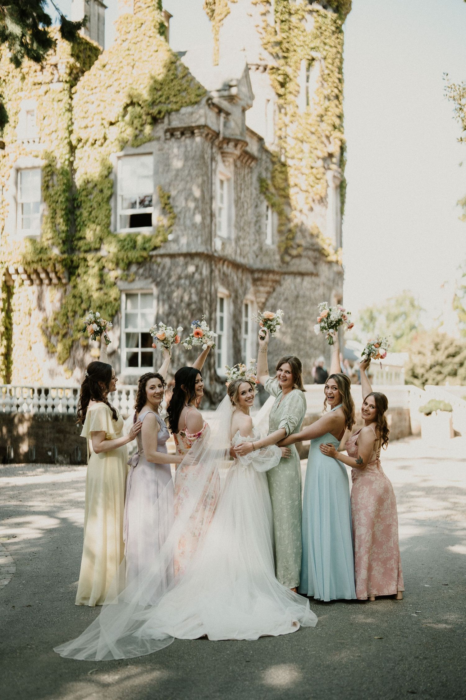 Wedding group poses elegantly against stone wall backdrop with climbing vines.