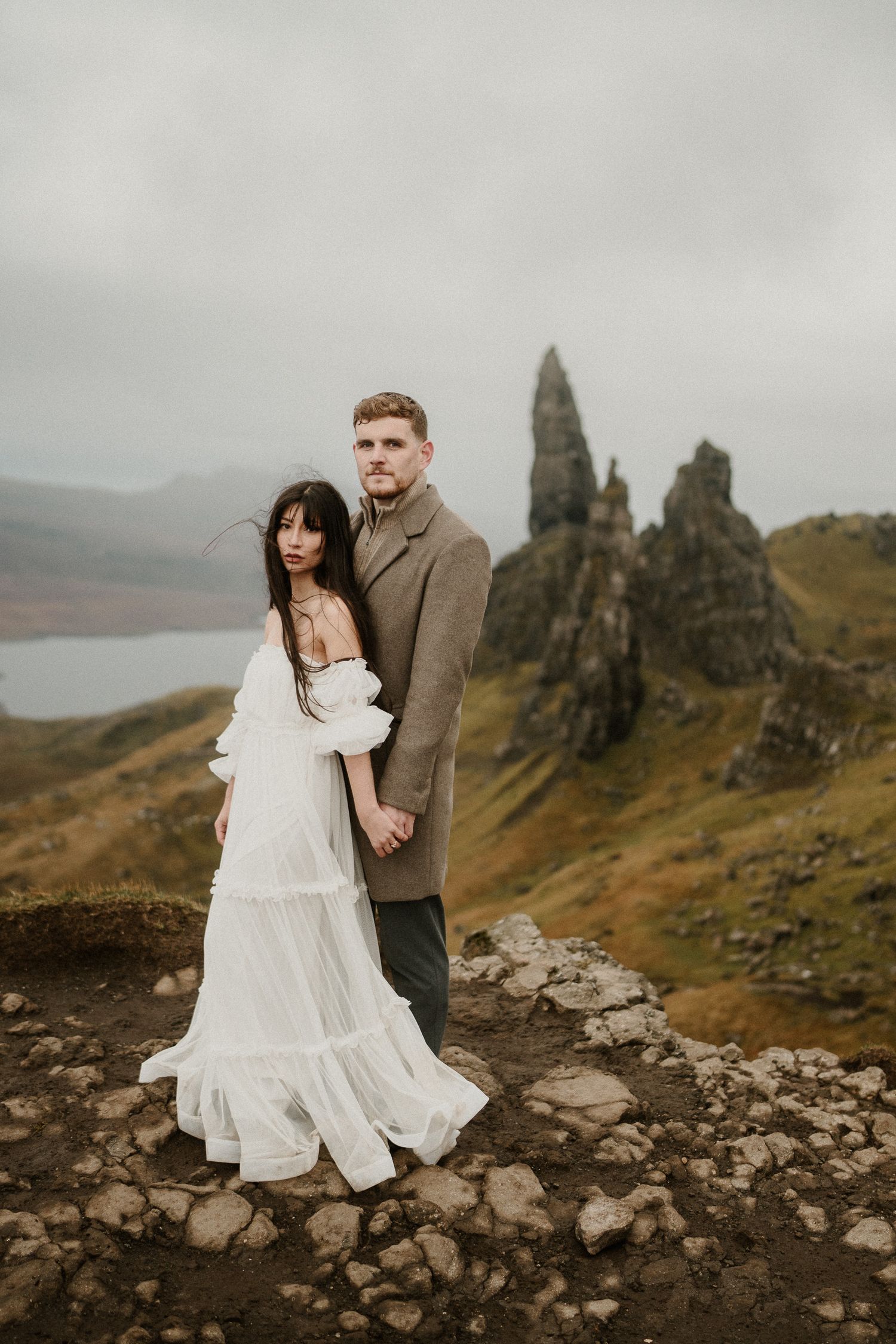 A romantic wedding couple poses against the dramatic backdrop of the Old Man of Storr in Scotland.