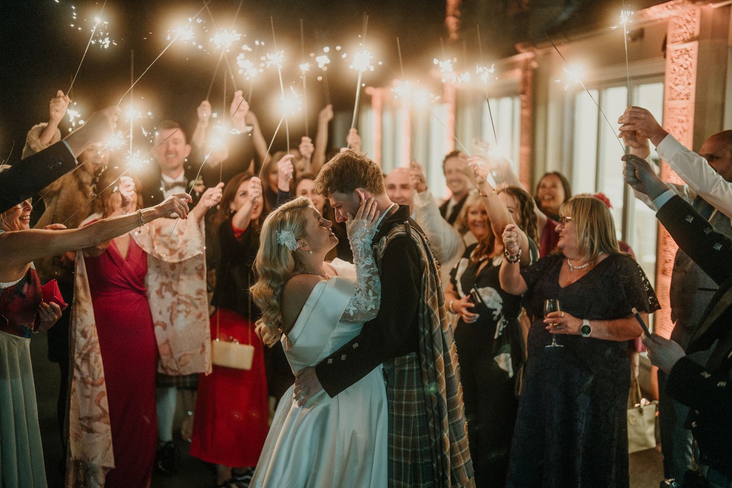 Sparklers illuminate joyful wedding celebration as guests surround dancing couple.