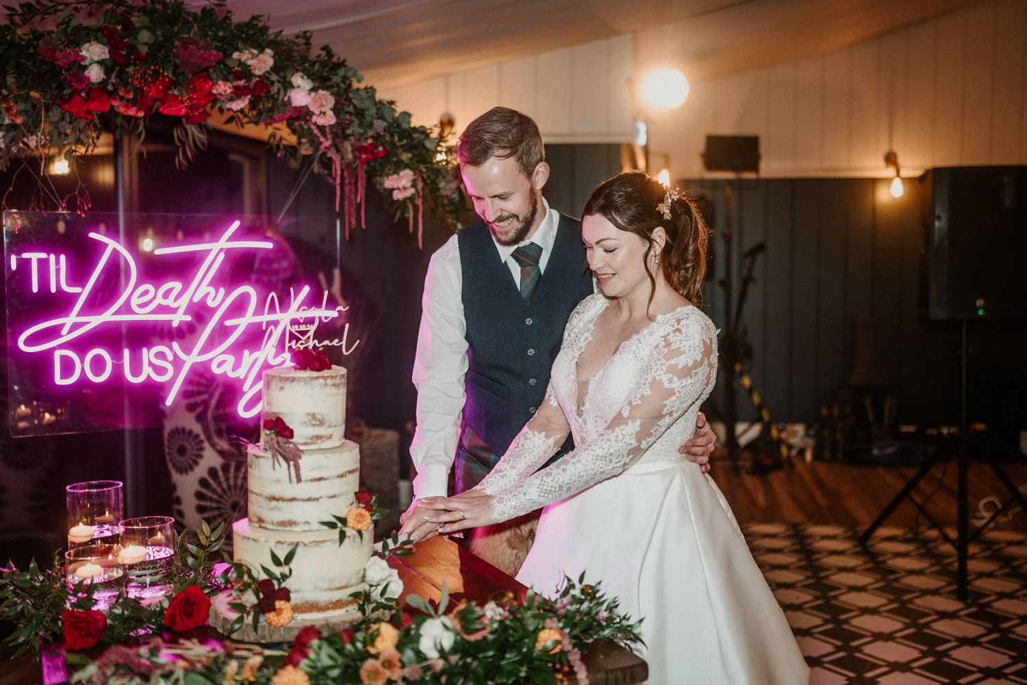 Wedding reception venue decorated with pink neon signs and floral arrangements.
