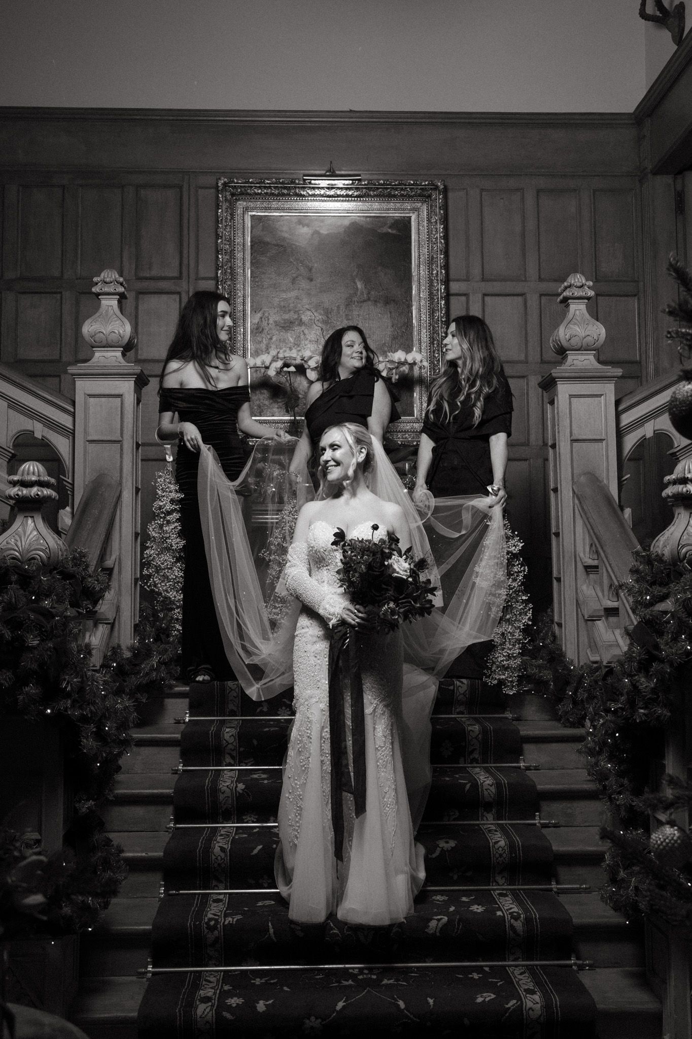 Black and white photo of wedding party on ornate staircase with classic architectural details.