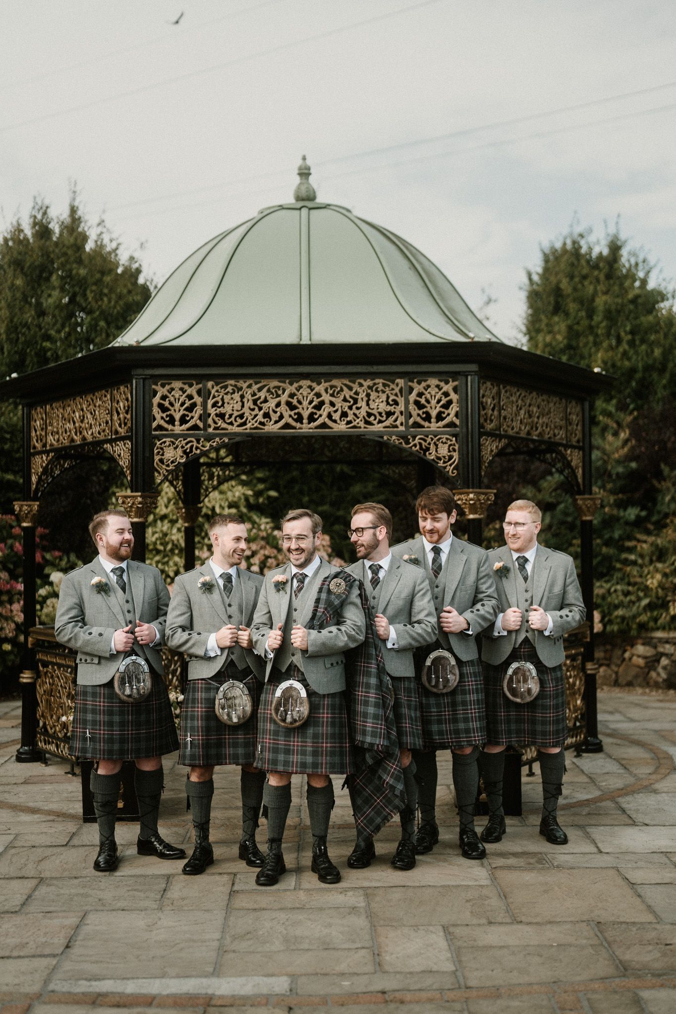 Groomsmen in traditional Scottish kilts posing together outdoors.