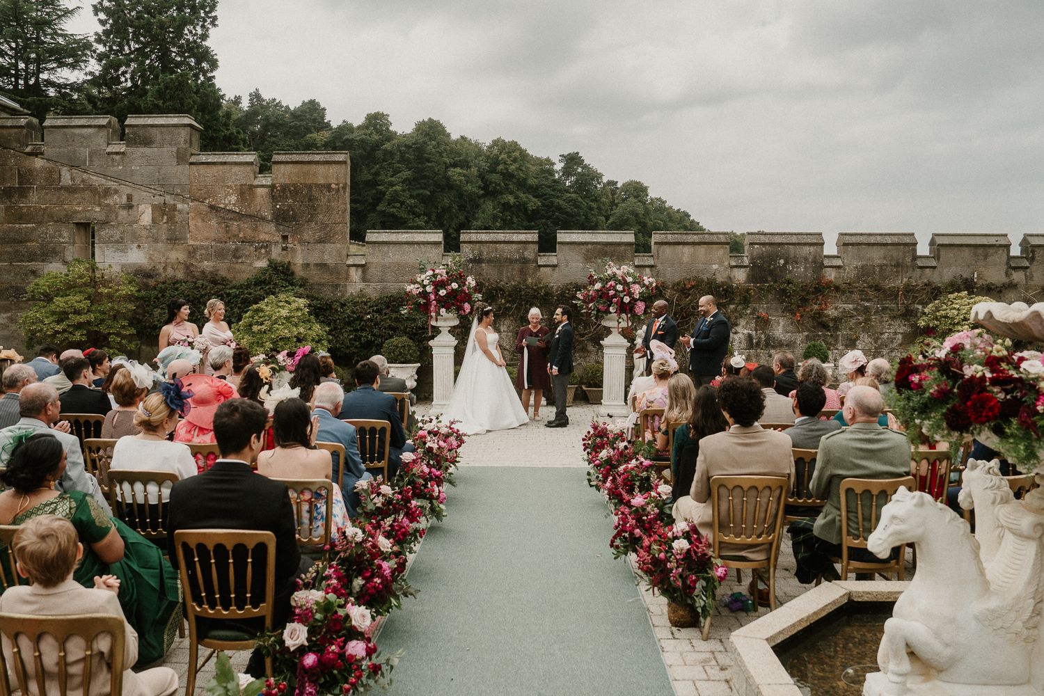 Stone terrace wedding venue decorated with lush floral arrangements and classic wooden chairs.
