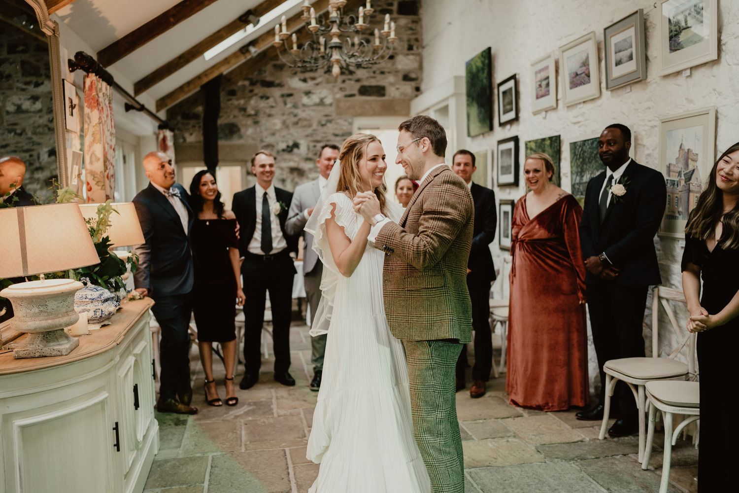 A couple shares their first dance in a rustic stone room with exposed beams and vintage decor.