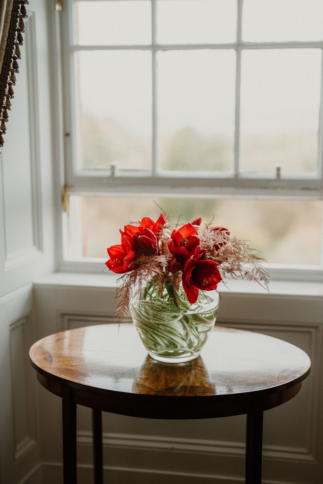 Modern round table by a window with a small glass vase holding red flowers.
