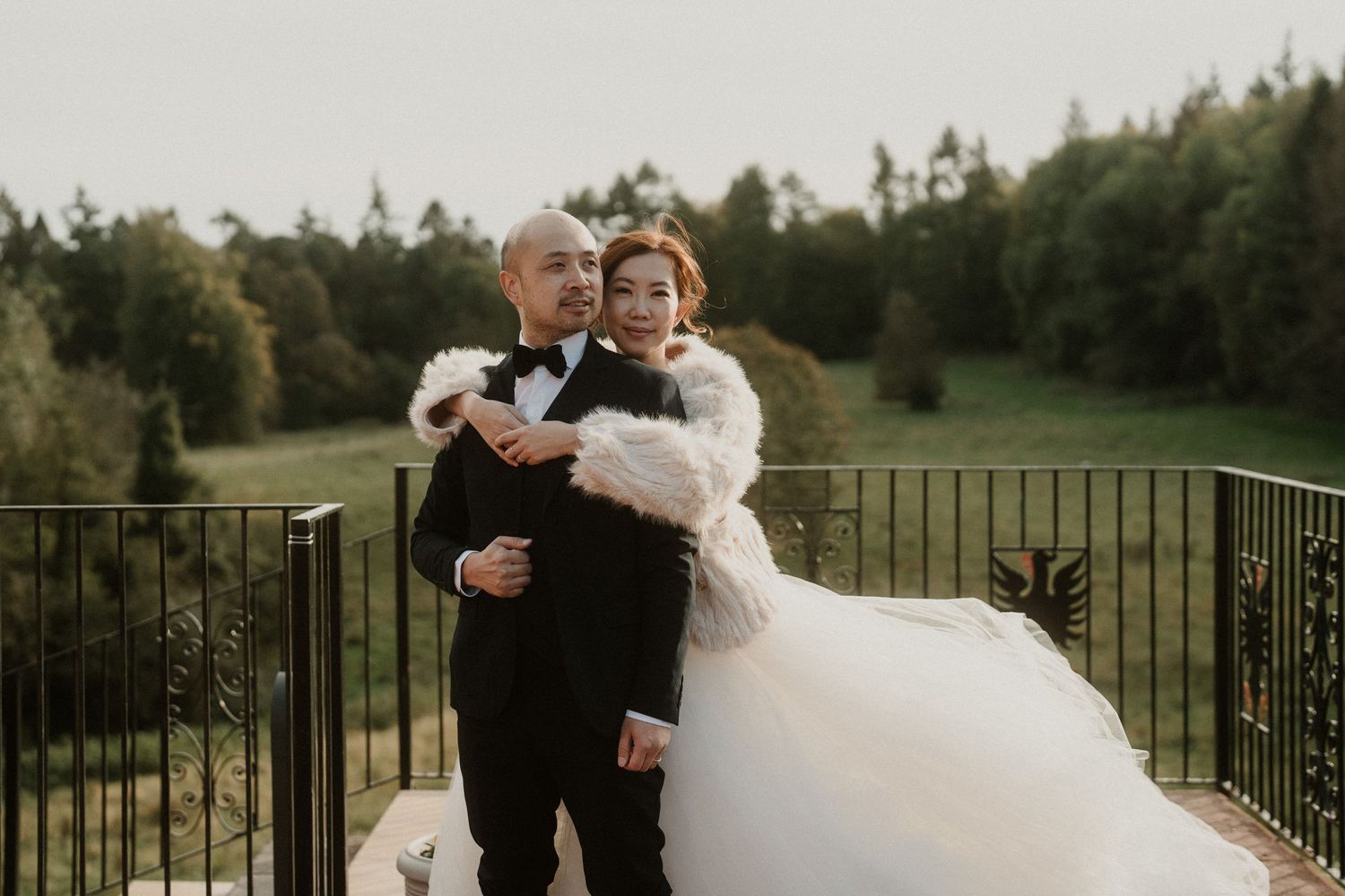 Couple embracing on a balcony overlooking a forest landscape at sunset.