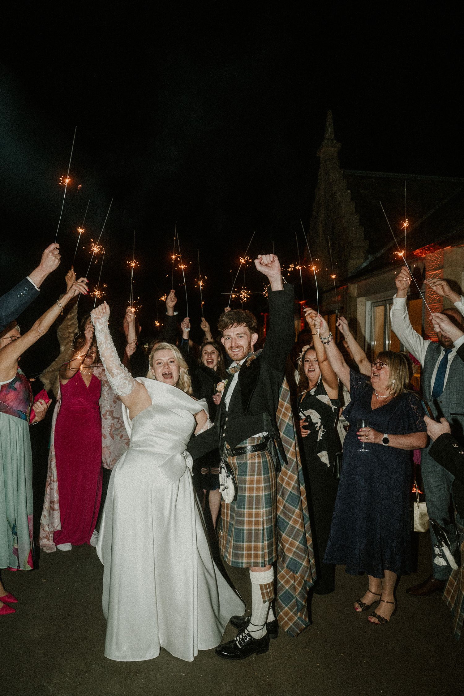 Wedding guests create a sparkler sendoff tunnel for the celebrating couple at night.