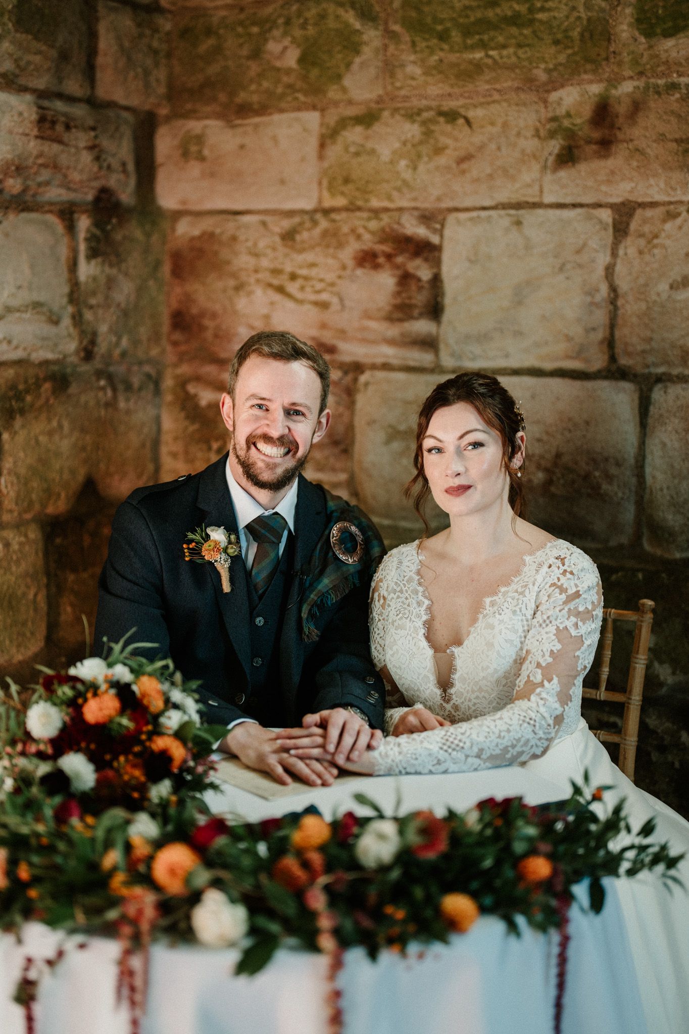 Couple at their wedding reception table decorated with orange and burgundy floral arrangements.