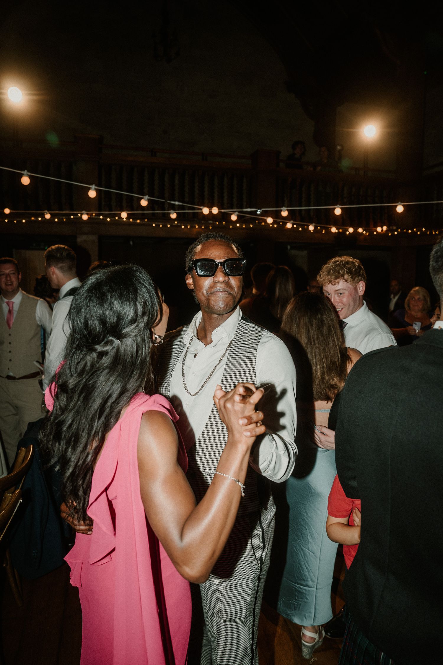 Wedding guests dancing and socializing at an evening reception with string light ambiance.