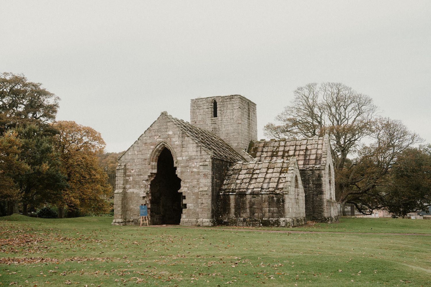 Ancient stone ruins and buildings stand in a green field under an overcast sky.