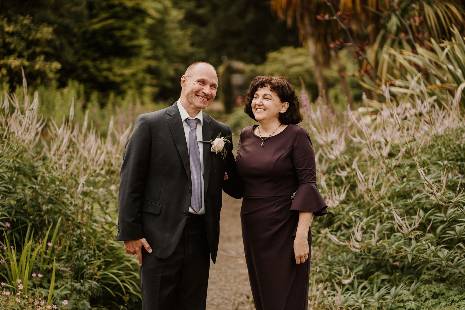 A couple shares a joyful moment together on a garden path surrounded by tall grasses.