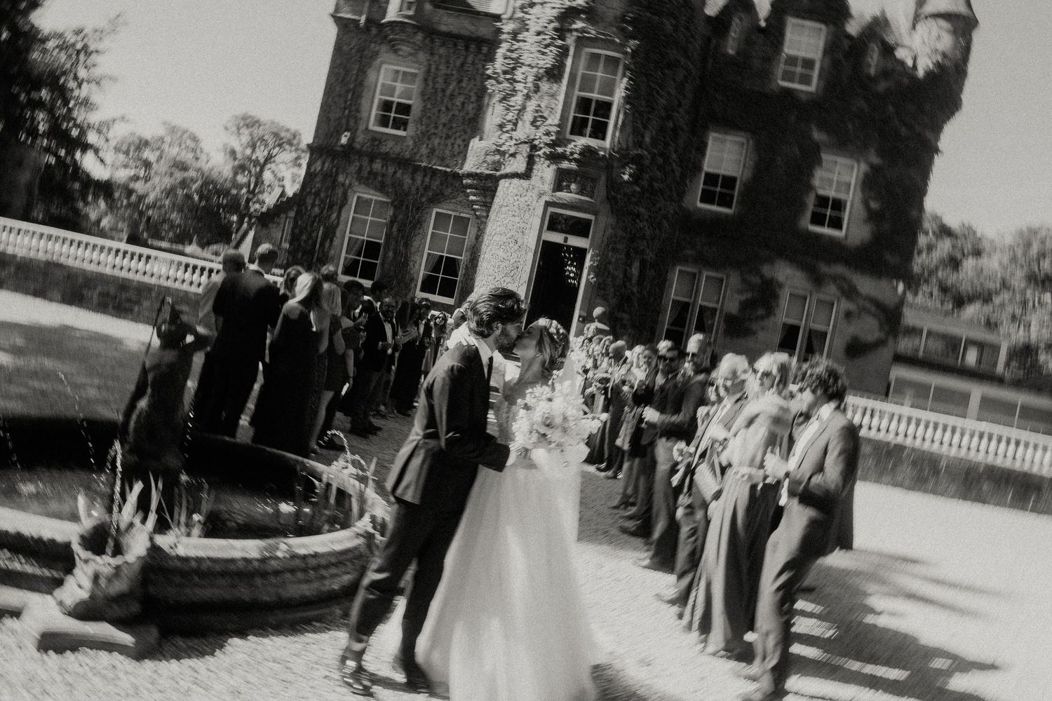 Black and white photo of wedding guests lining up outside a historic building.