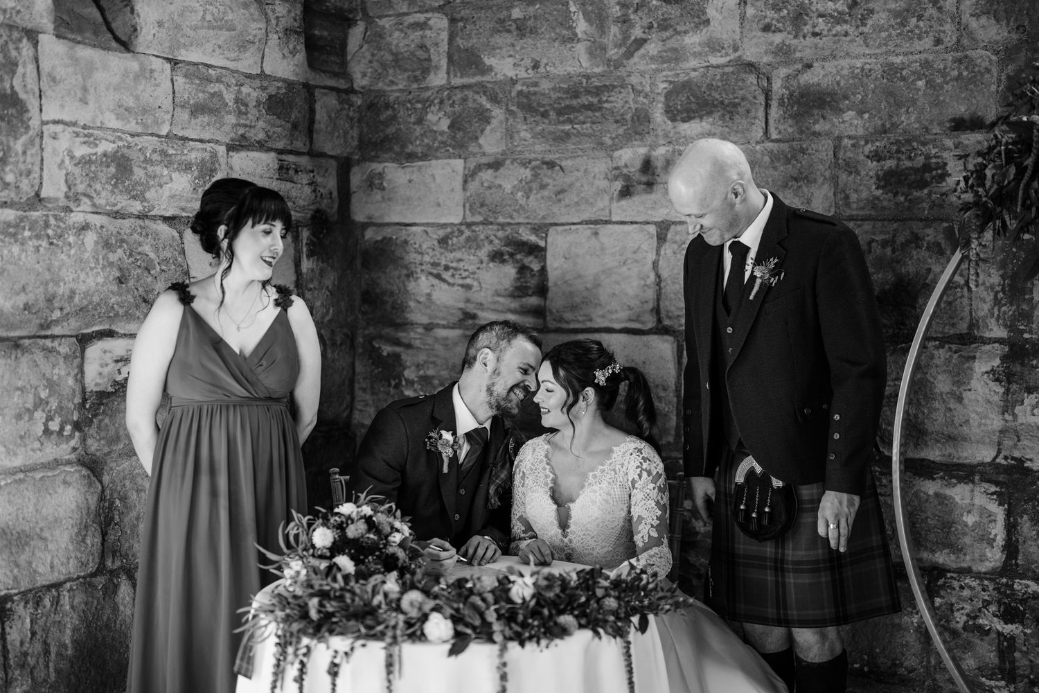 Black and white portrait of a wedding party in traditional Scottish attire at a stone castle.
