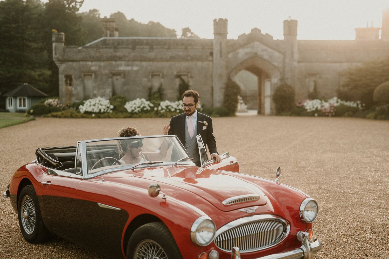 Beautiful red classic convertible car displayed on castle grounds during wedding celebration.