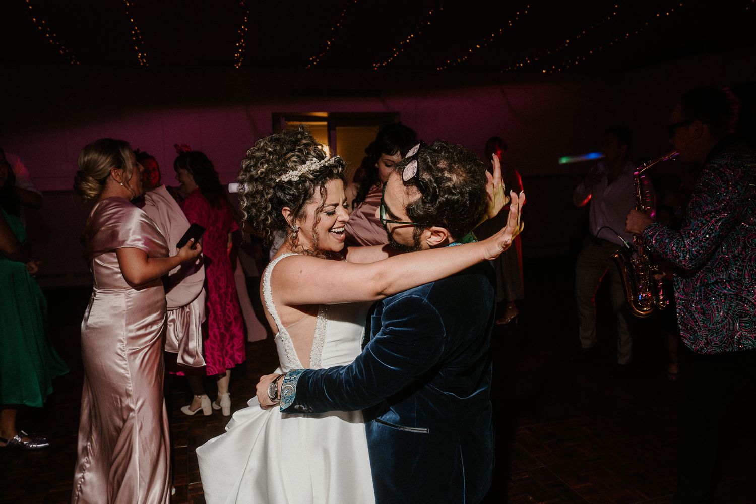 Couples dancing together at wedding reception under moody purple lighting.