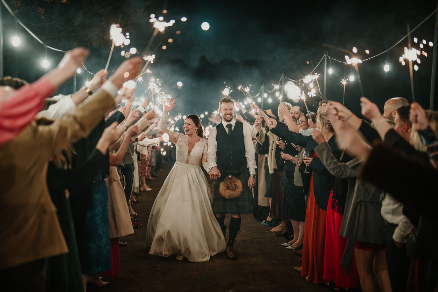 Guests line up with sparklers creating a magical nighttime wedding exit pathway.