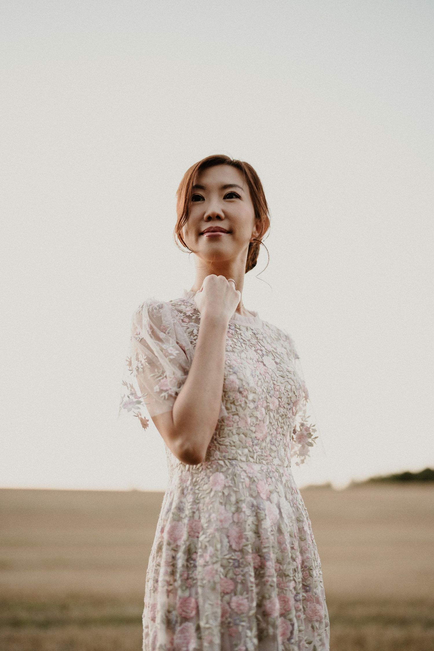 A person in a delicate lace dress poses against a rural landscape backdrop.