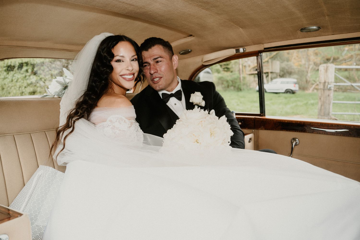 Newlyweds share intimate moments inside vintage car during wedding day.