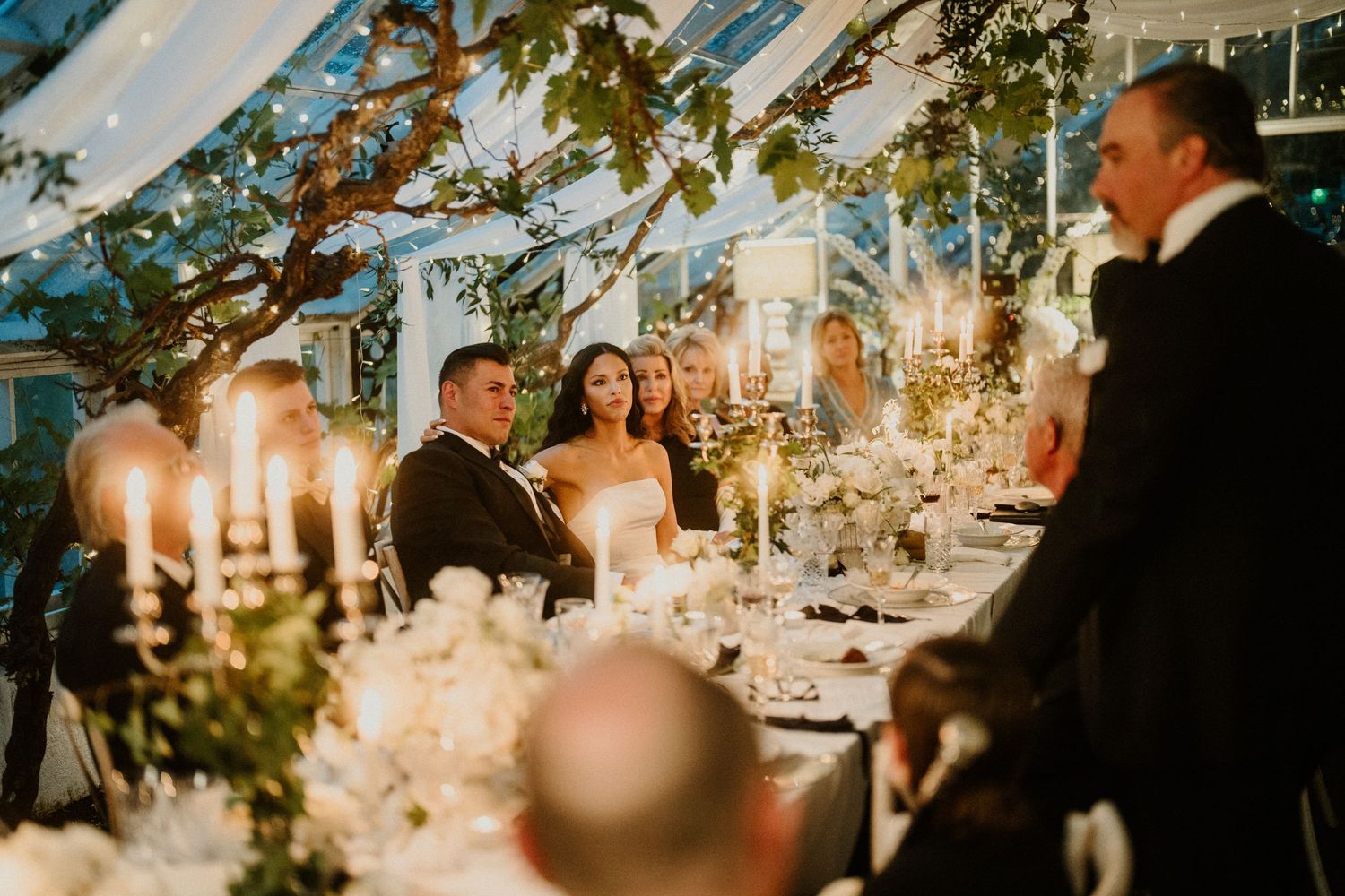 Wedding guests gather around candlelit tables during an evening reception.