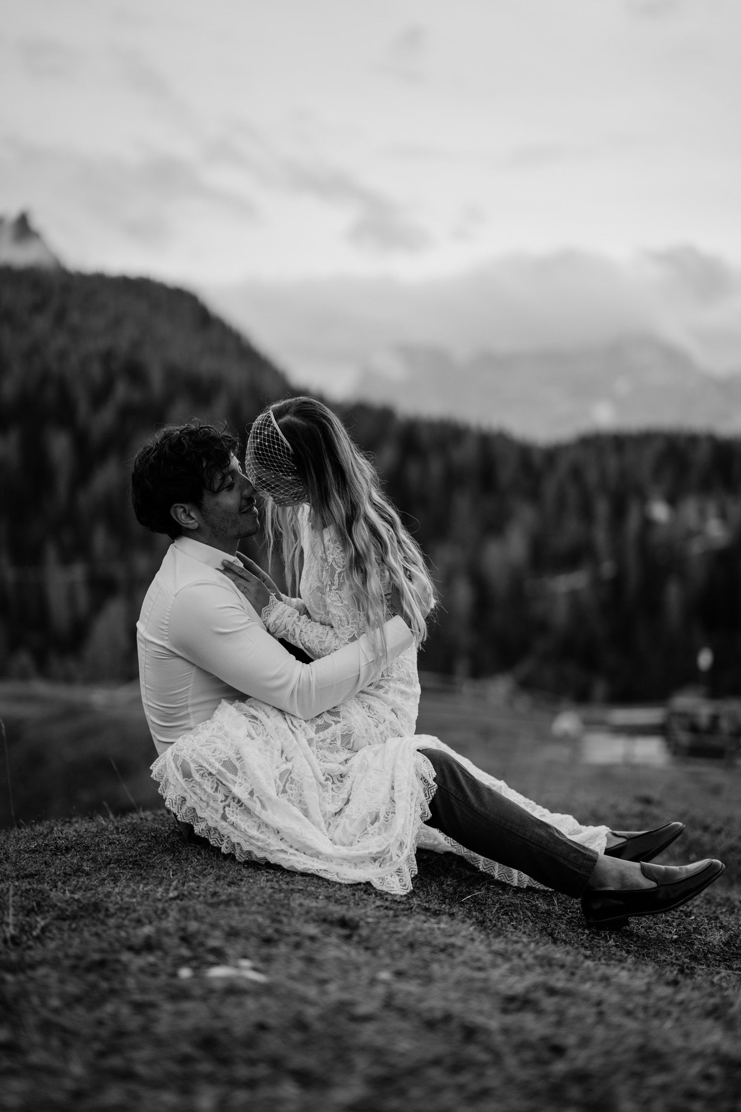 Black and white photo of a couple in white clothing sharing a tender moment on a mountainside.