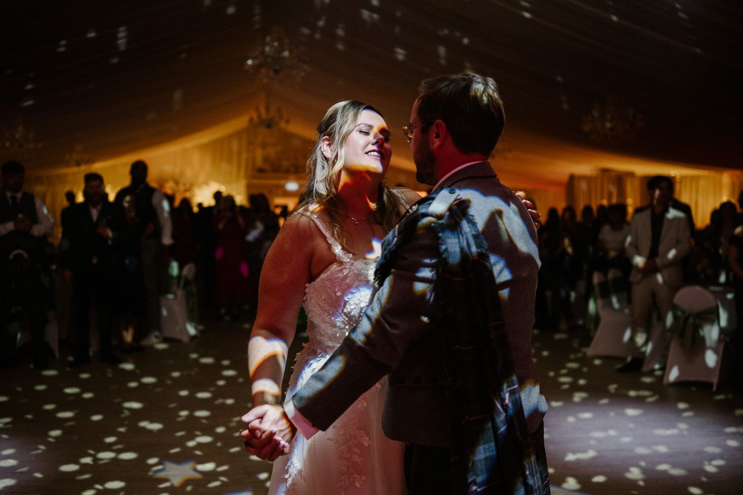 Dimly lit wedding reception dance floor with guests celebrating in formal attire.