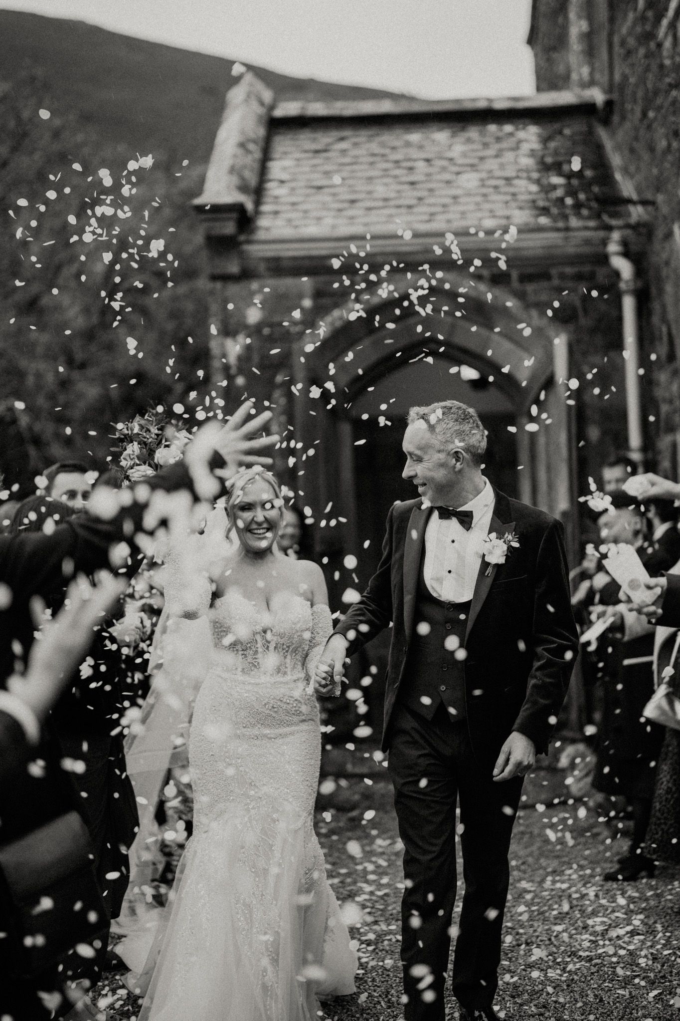 Black and white capture of wedding party celebrating with confetti outside church.