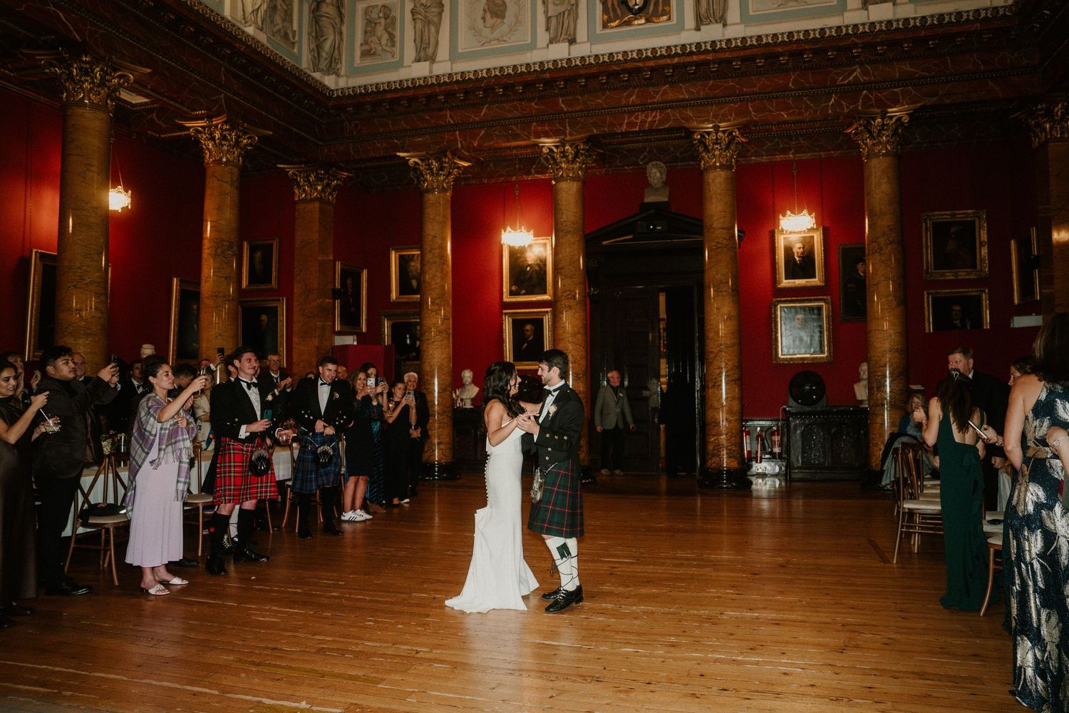 Elegant ballroom wedding reception with guests dancing under ornate architectural details.