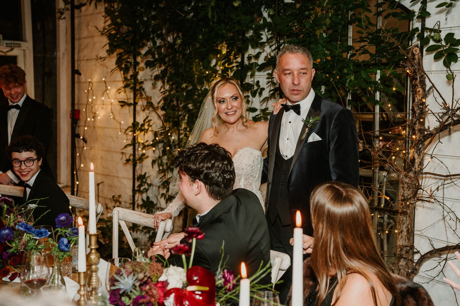 Wedding celebration in an indoor venue decorated with climbing vines and candlelight.