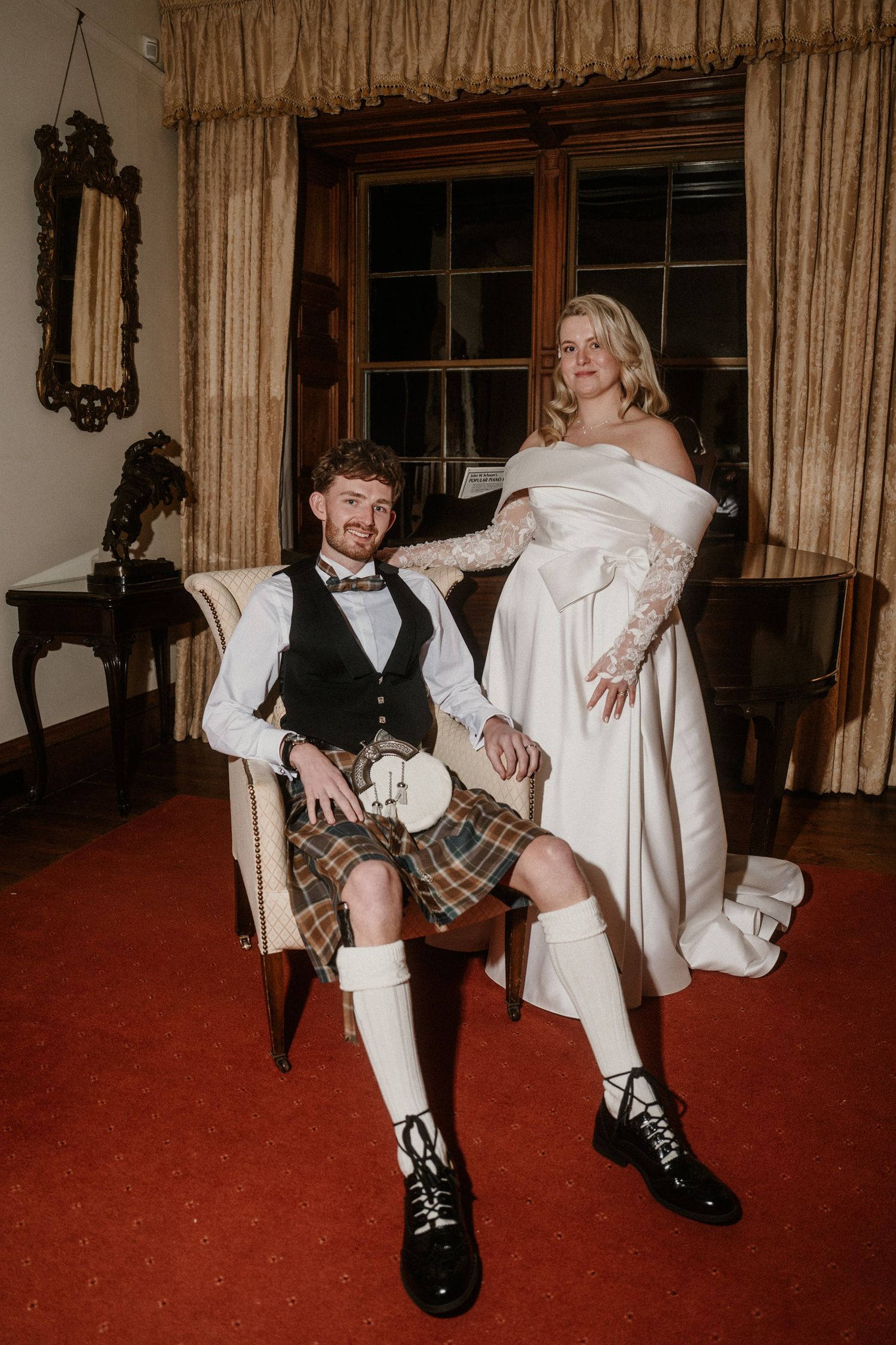 A couple shares a playful moment during their wedding, with the groom wearing a traditional Scottish kilt on a red carpet.