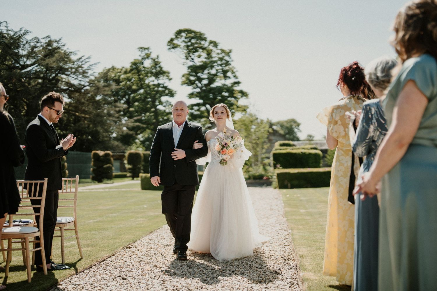 Wedding ceremony setup with elegant white pedestals and floral arrangements on a sunny outdoor lawn.