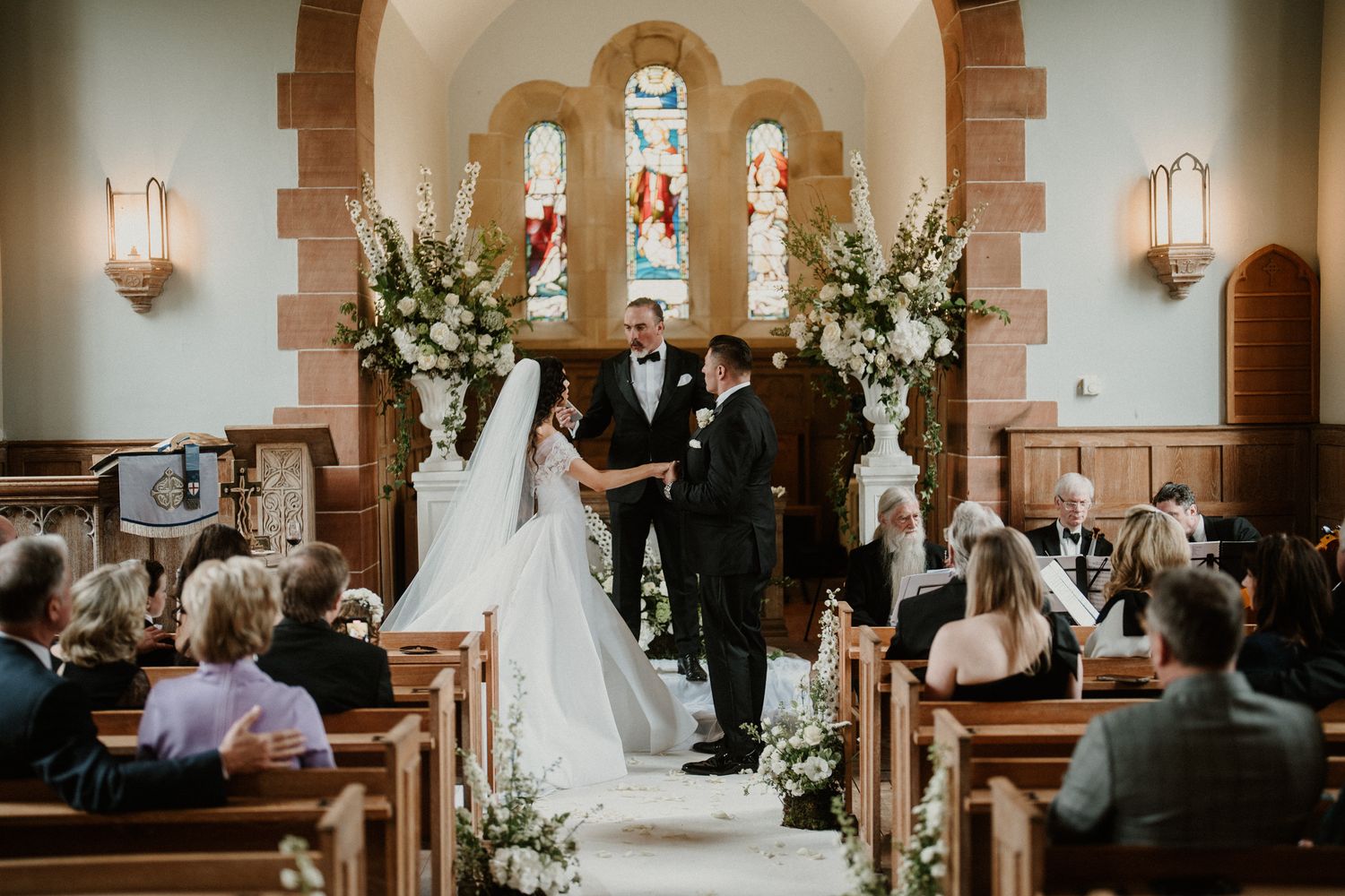 A traditional church wedding ceremony with white floral decorations and stained glass windows.