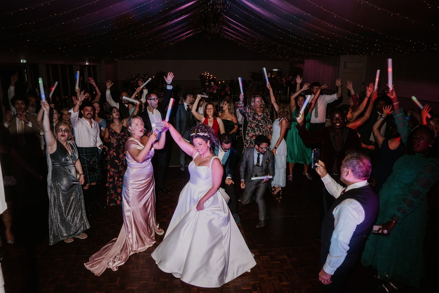 Wide angle shot of a crowded wedding dance floor with purple and blue lighting effects.