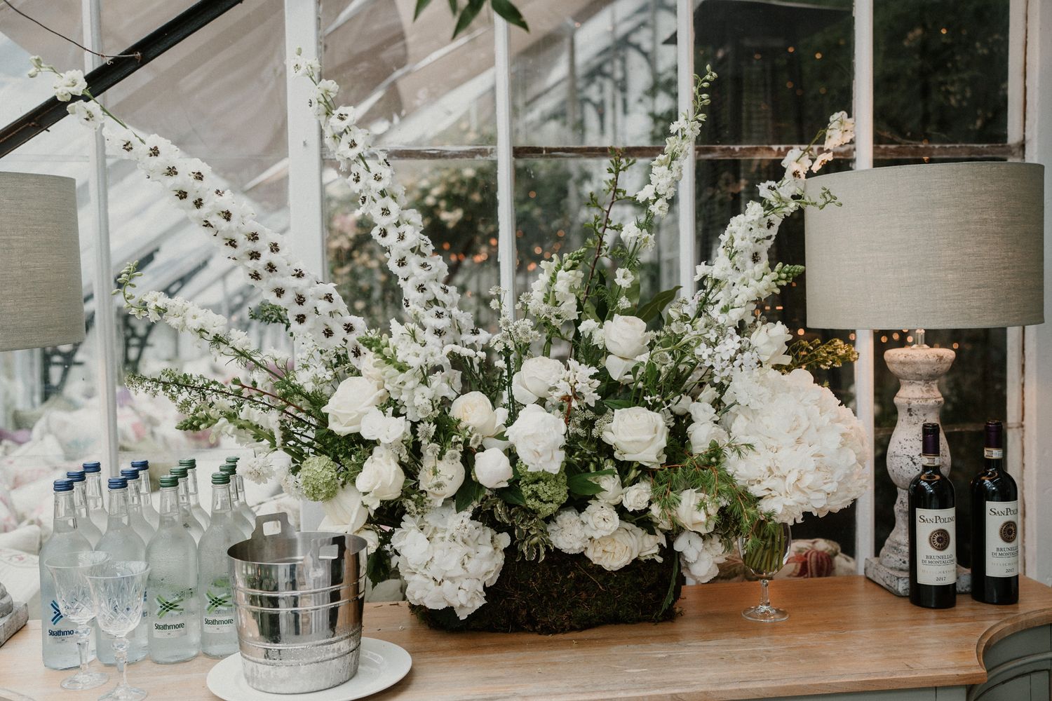 Lush white floral arrangement with spring blossoms on wedding reception bar.