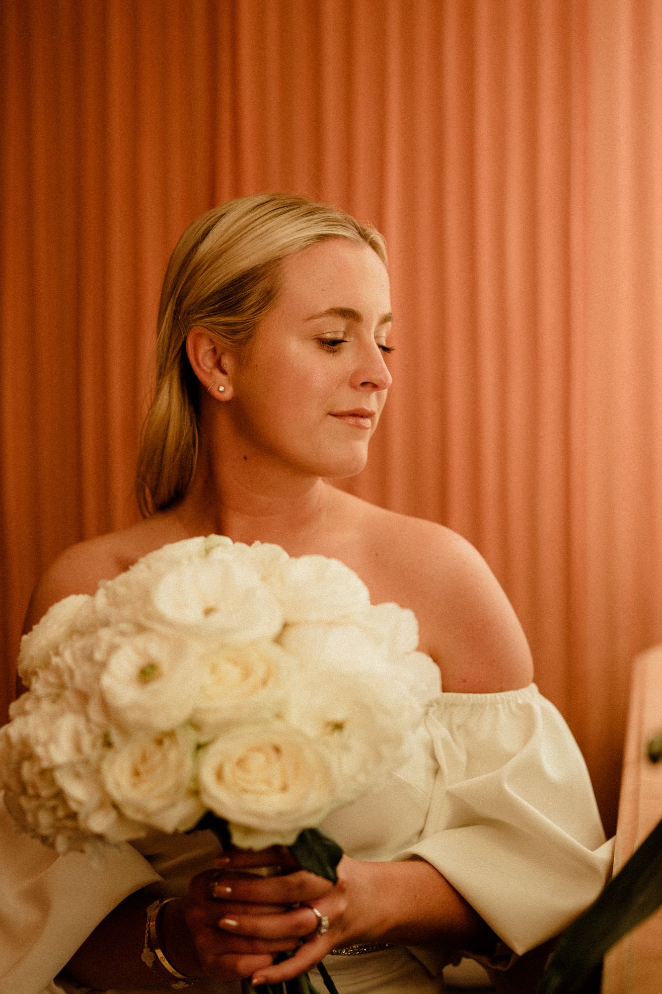 Artistic series of a bride holding a luxurious bouquet of white roses against a coral-colored backdrop.
