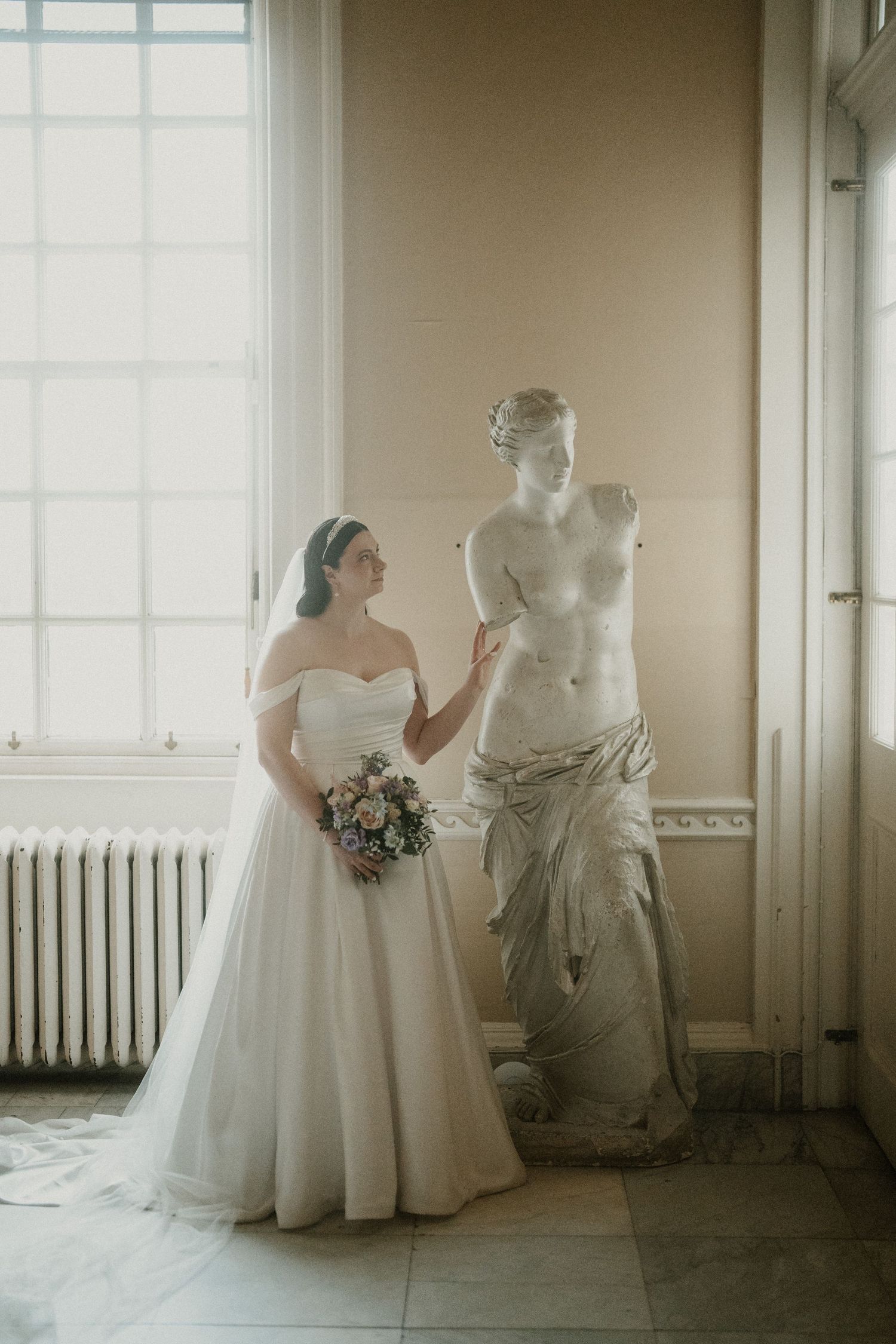 Artistic bridal gown display in bright sunlit room with classical interior details.