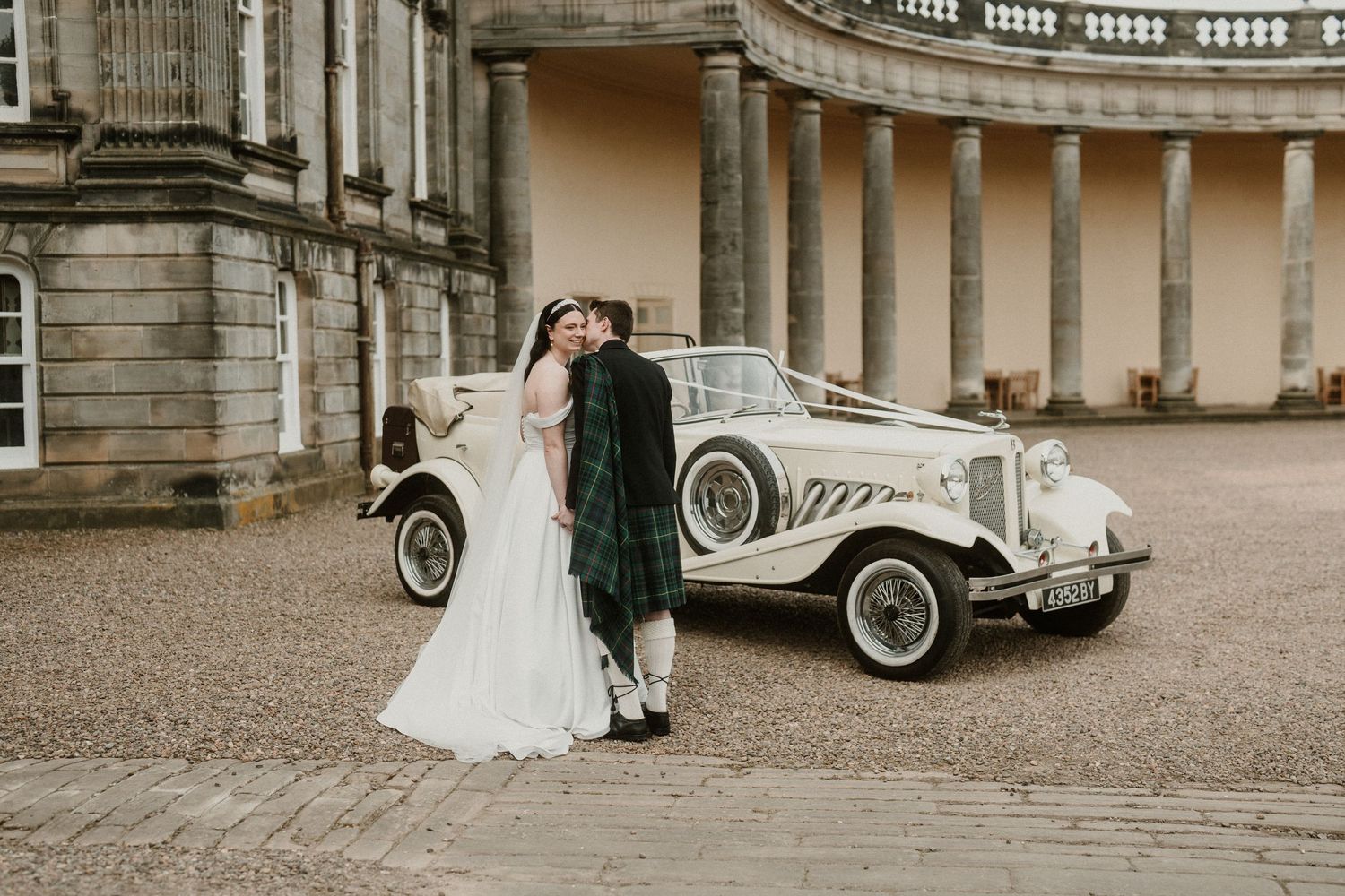 Elegant white vintage car parked in front of historic stone building during wedding.