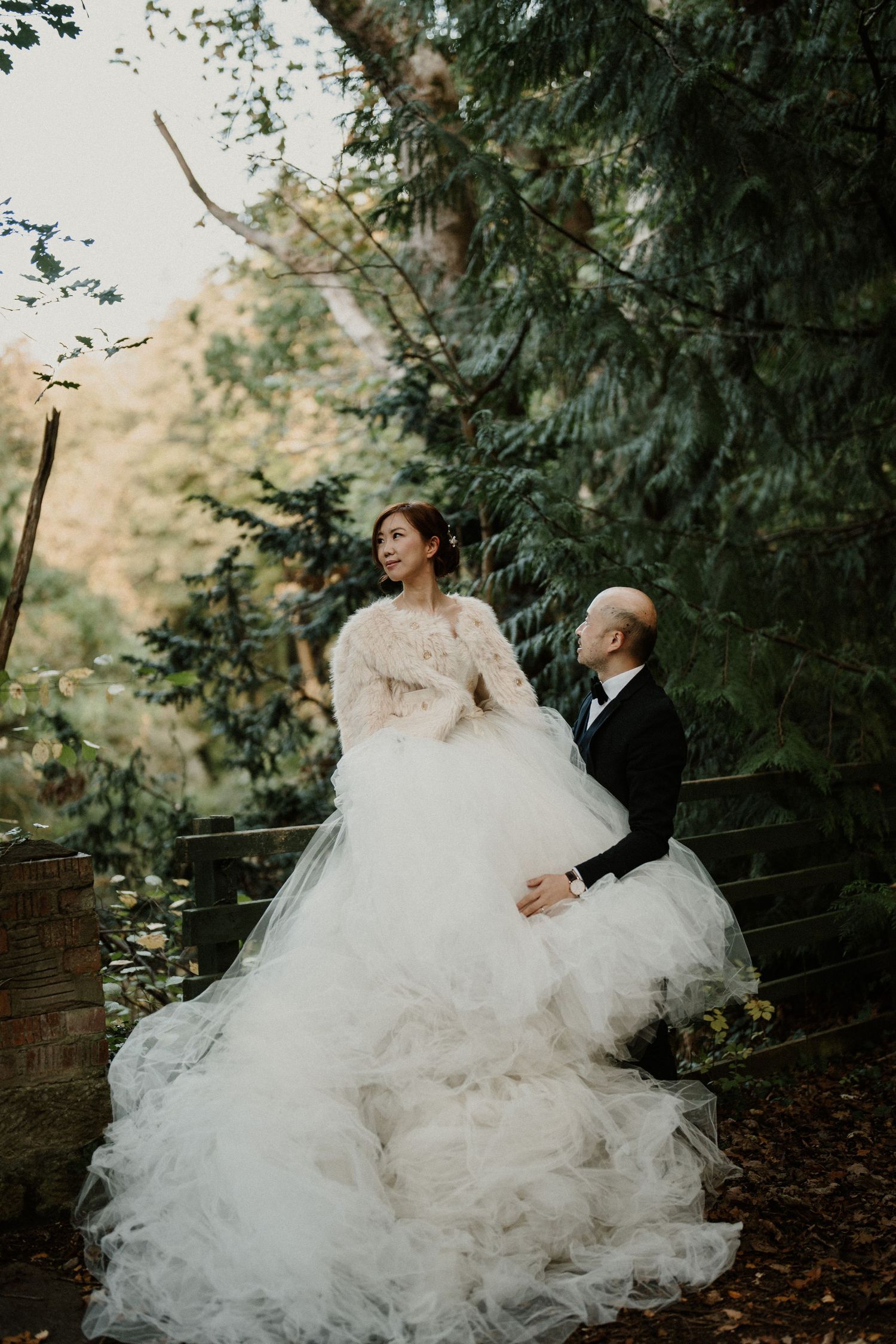 A couple shares a romantic moment on a stone bench surrounded by lush greenery.