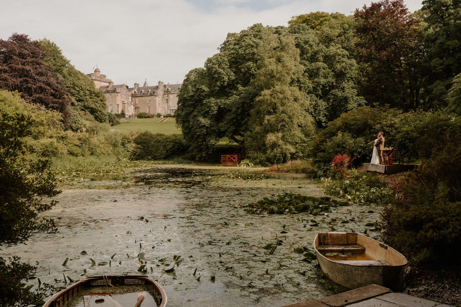 A scenic pond view with lily pads and a historic building in the background.