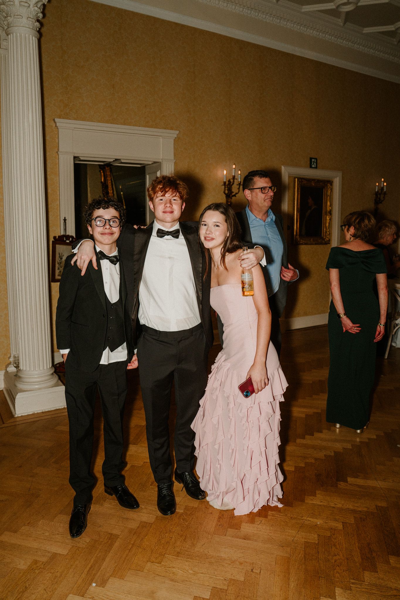 Wedding guests in formal attire enjoying themselves on a wooden dance floor at an elegant venue.