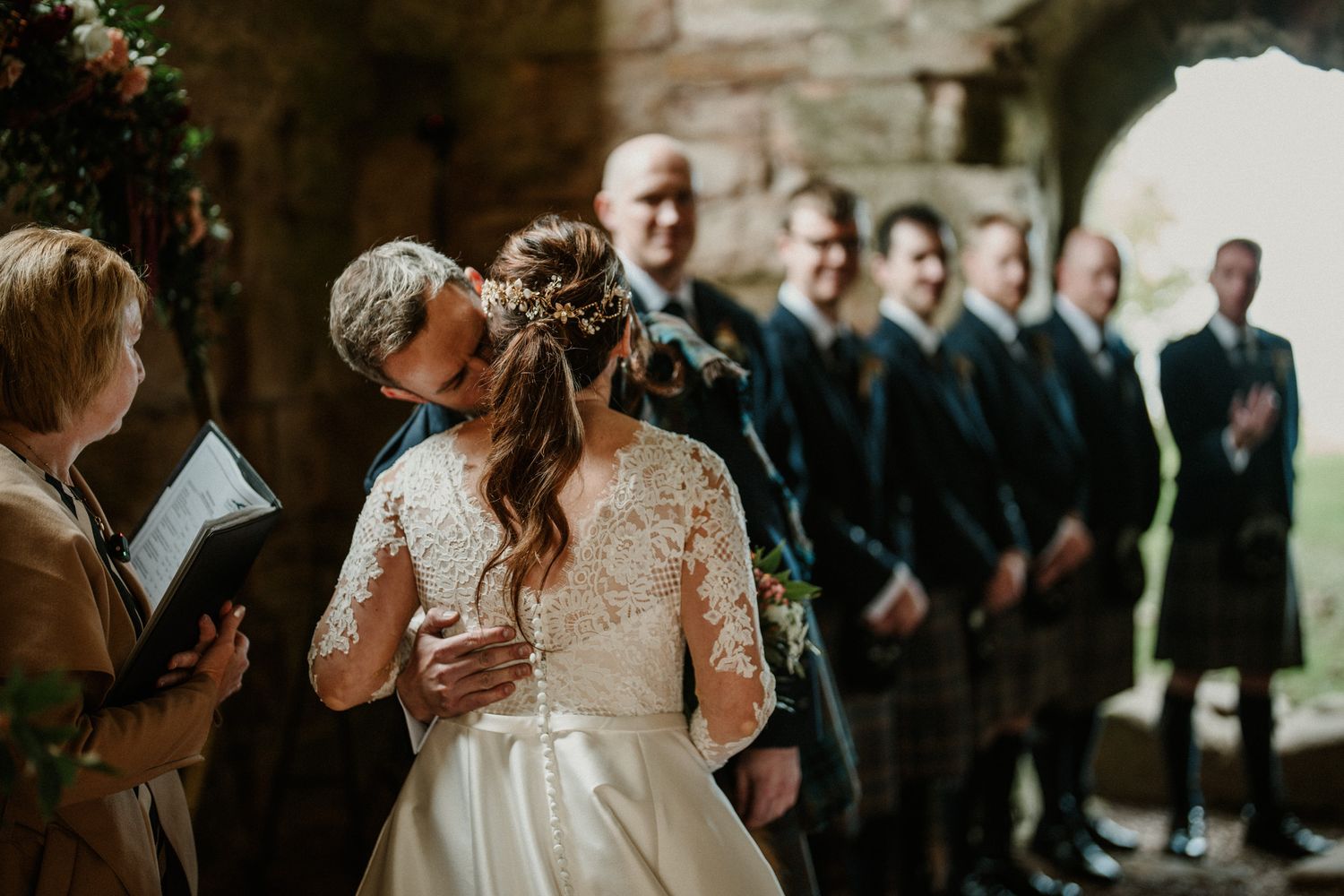 Wedding party gathered in historic stone venue with romantic lighting and floral decor.