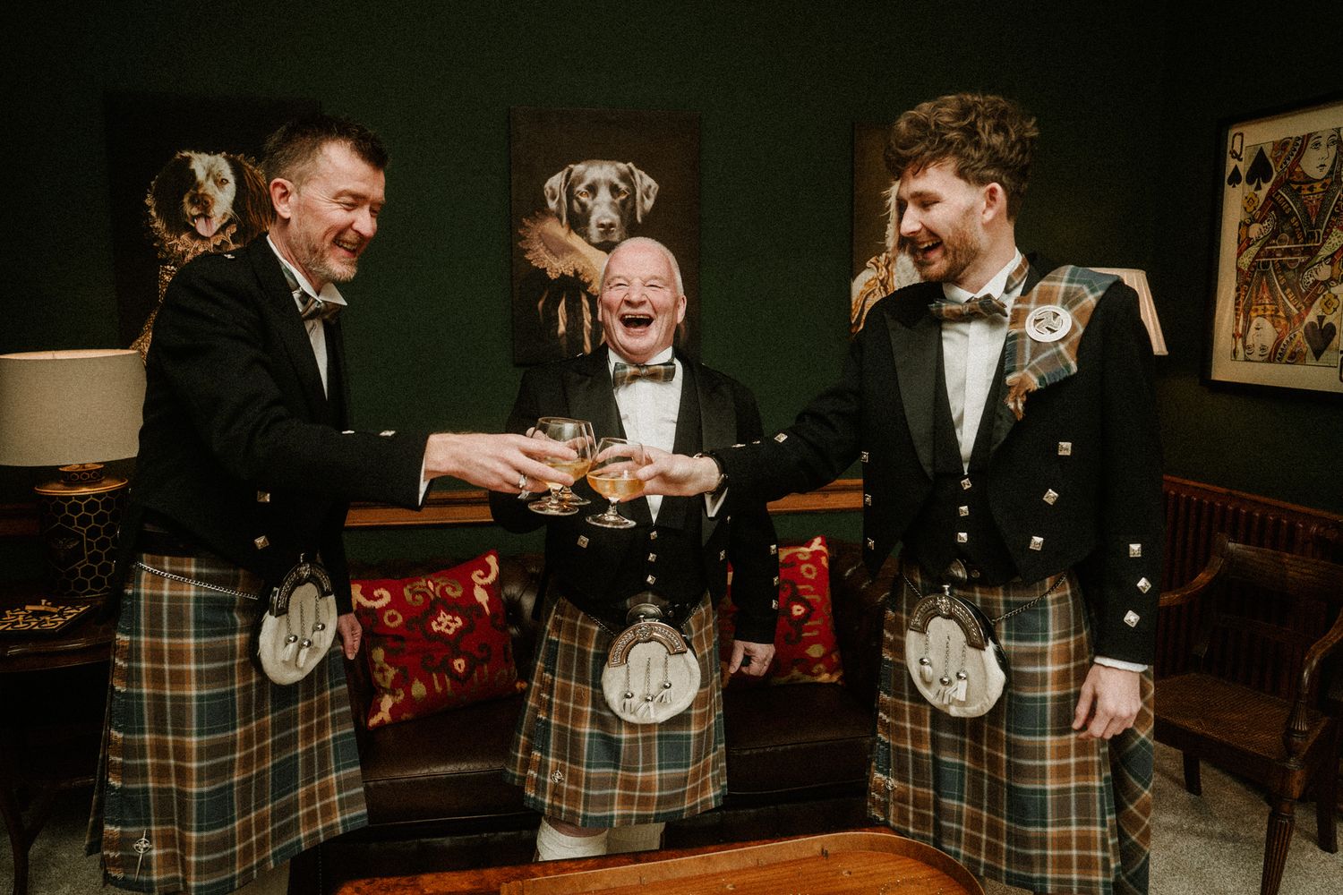 Three men in traditional Scottish kilts sharing drinks in a dimly lit room.