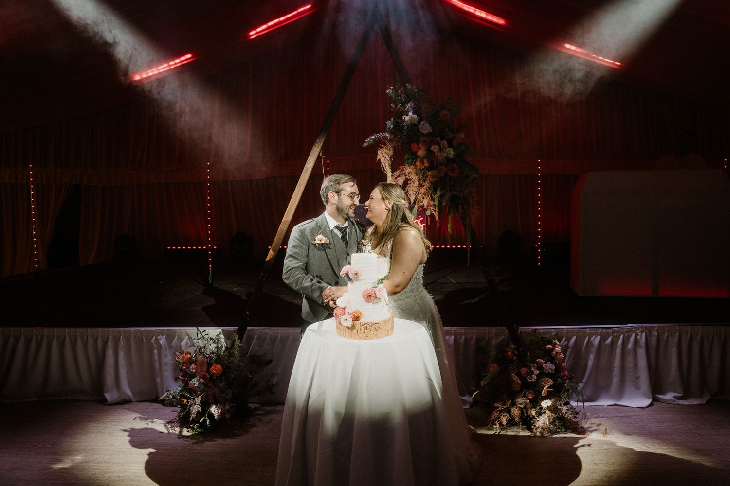 Couple dancing in a romantic spotlight during wedding reception with dramatic red lighting effects.