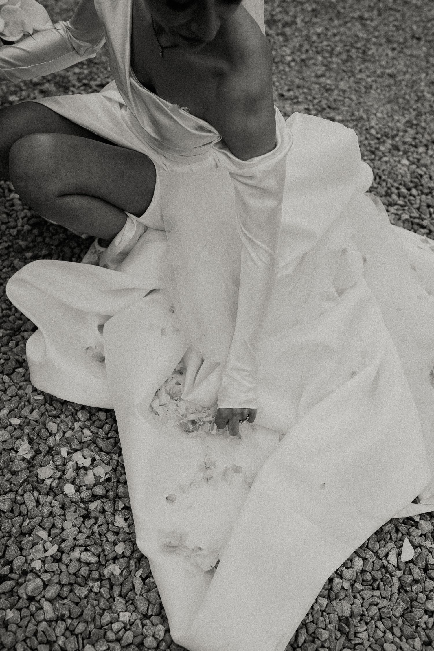 White wedding dress spread out on gravel ground in artistic black and white photography.