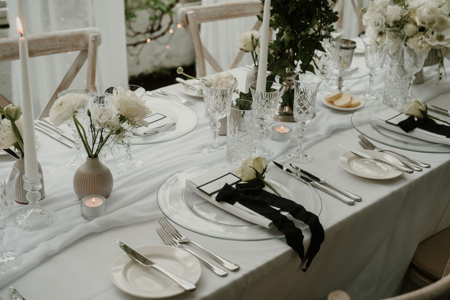 White wedding reception table with elegant place settings and black ribbon accents.