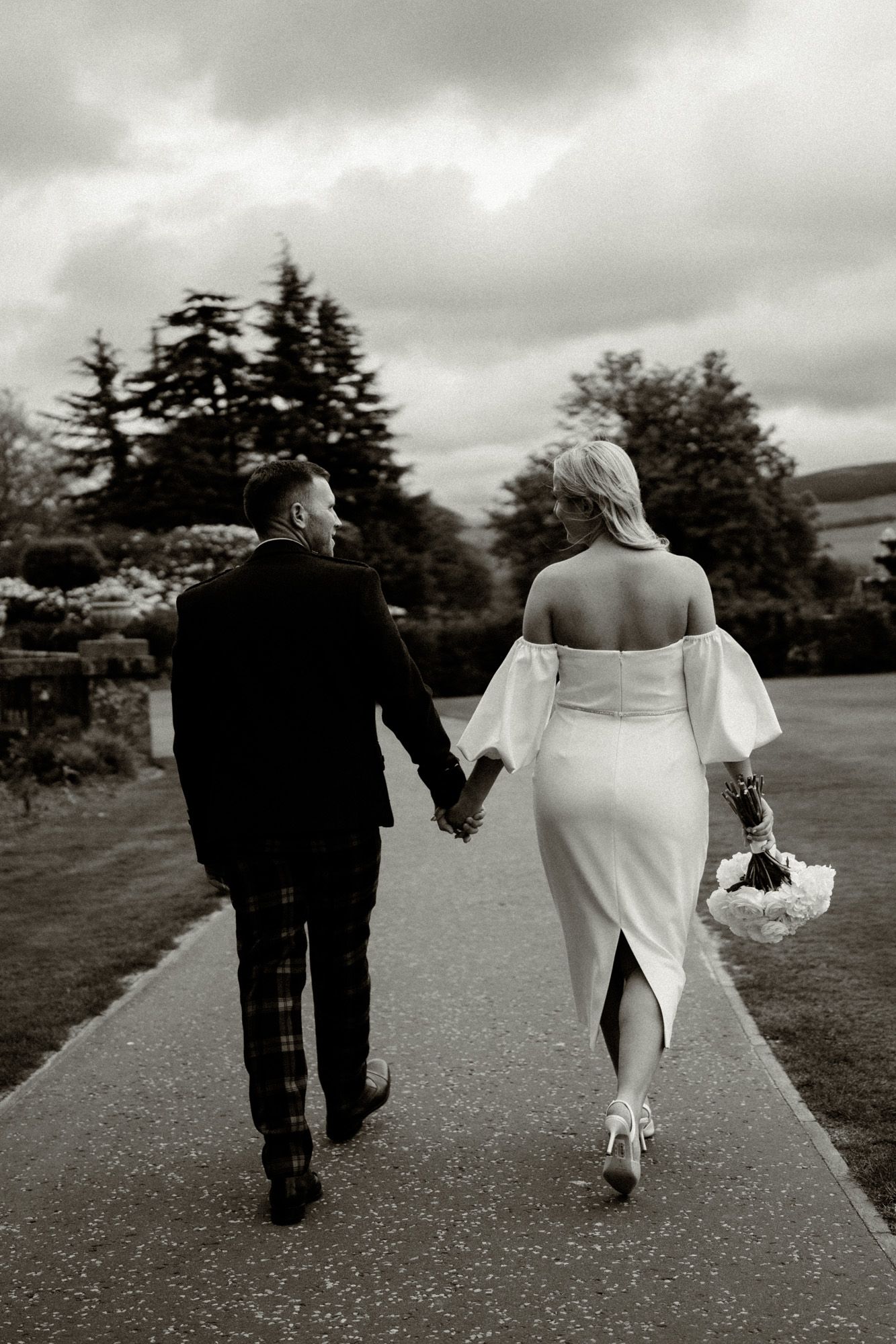 Couple walking down path with cloudy sky and trees in background.