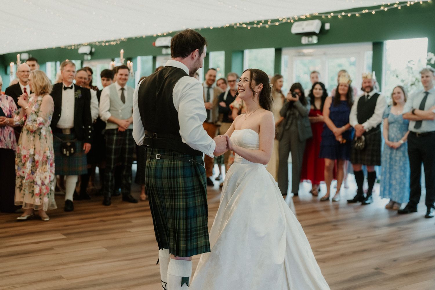 Bride and groom share first dance at Scottish wedding, groom wearing traditional tartan kilt in elegant venue.