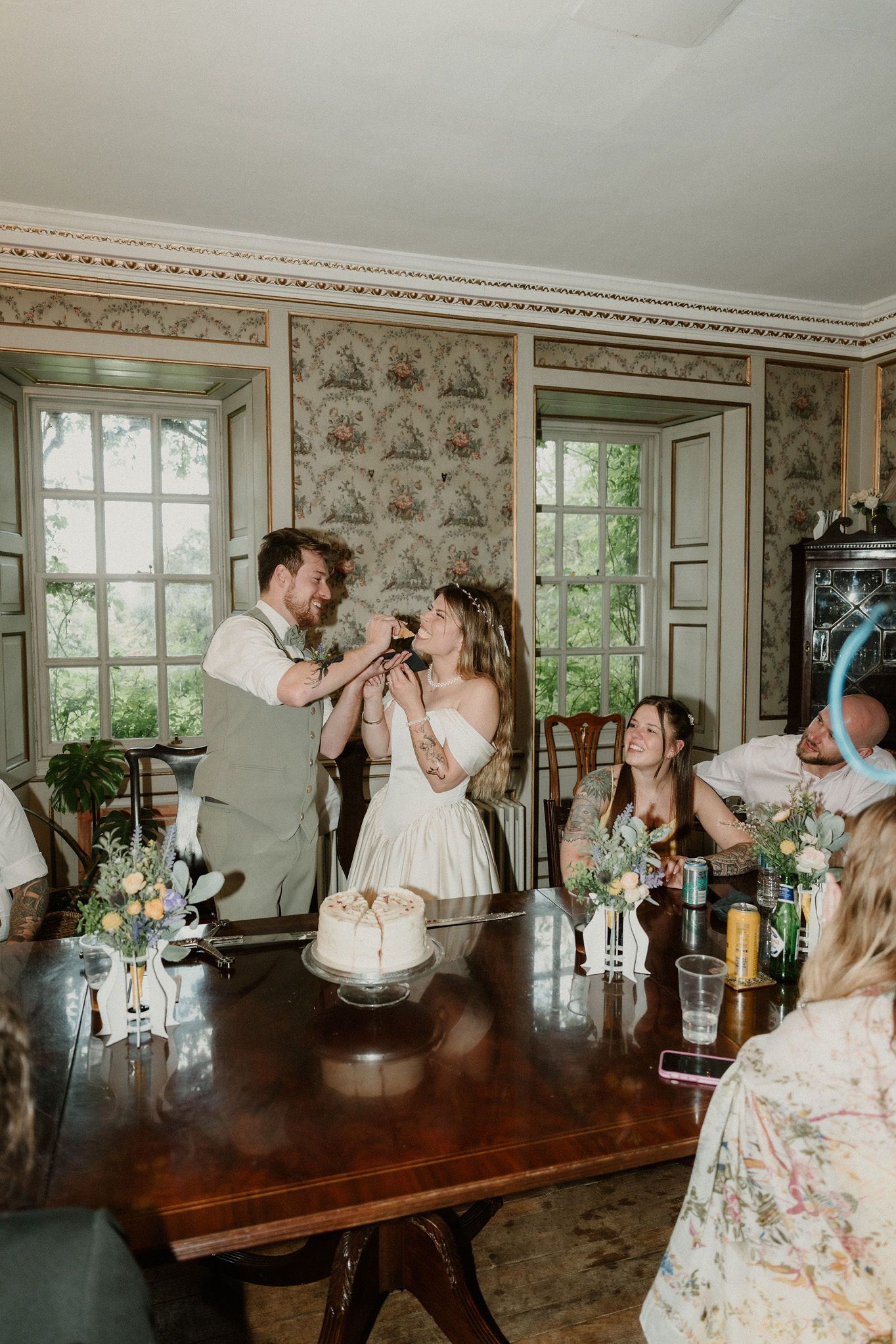 Bride and groom share a joyful toast at their intimate wedding reception in an elegant floral wallpapered room.
