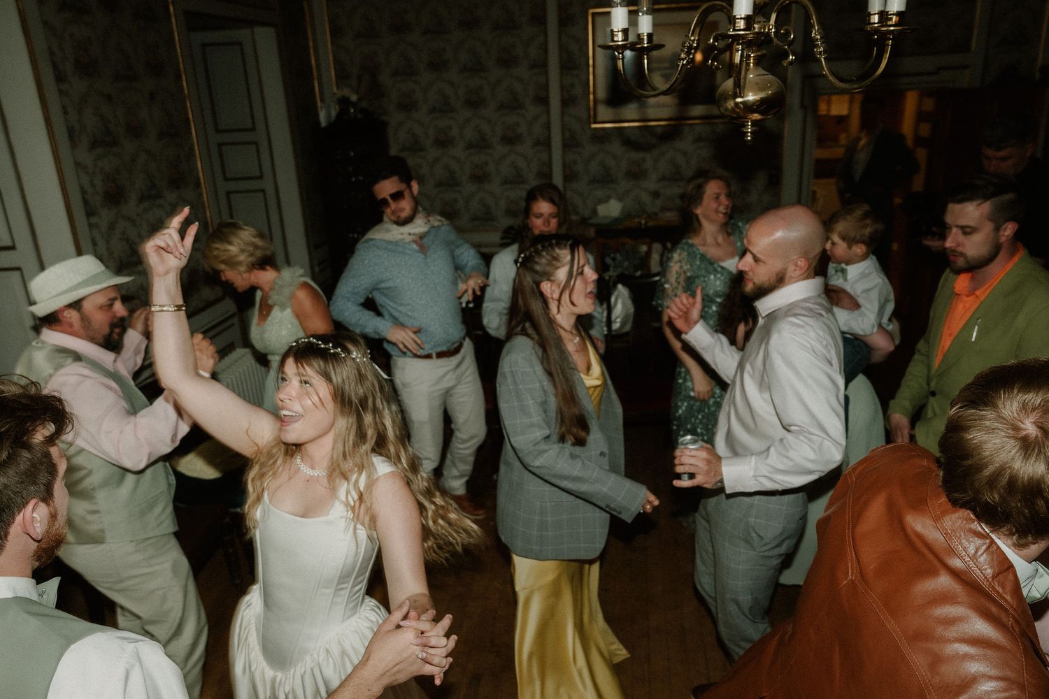 Guests dancing joyfully at a wedding reception in an elegant vintage venue with chandelier lighting.