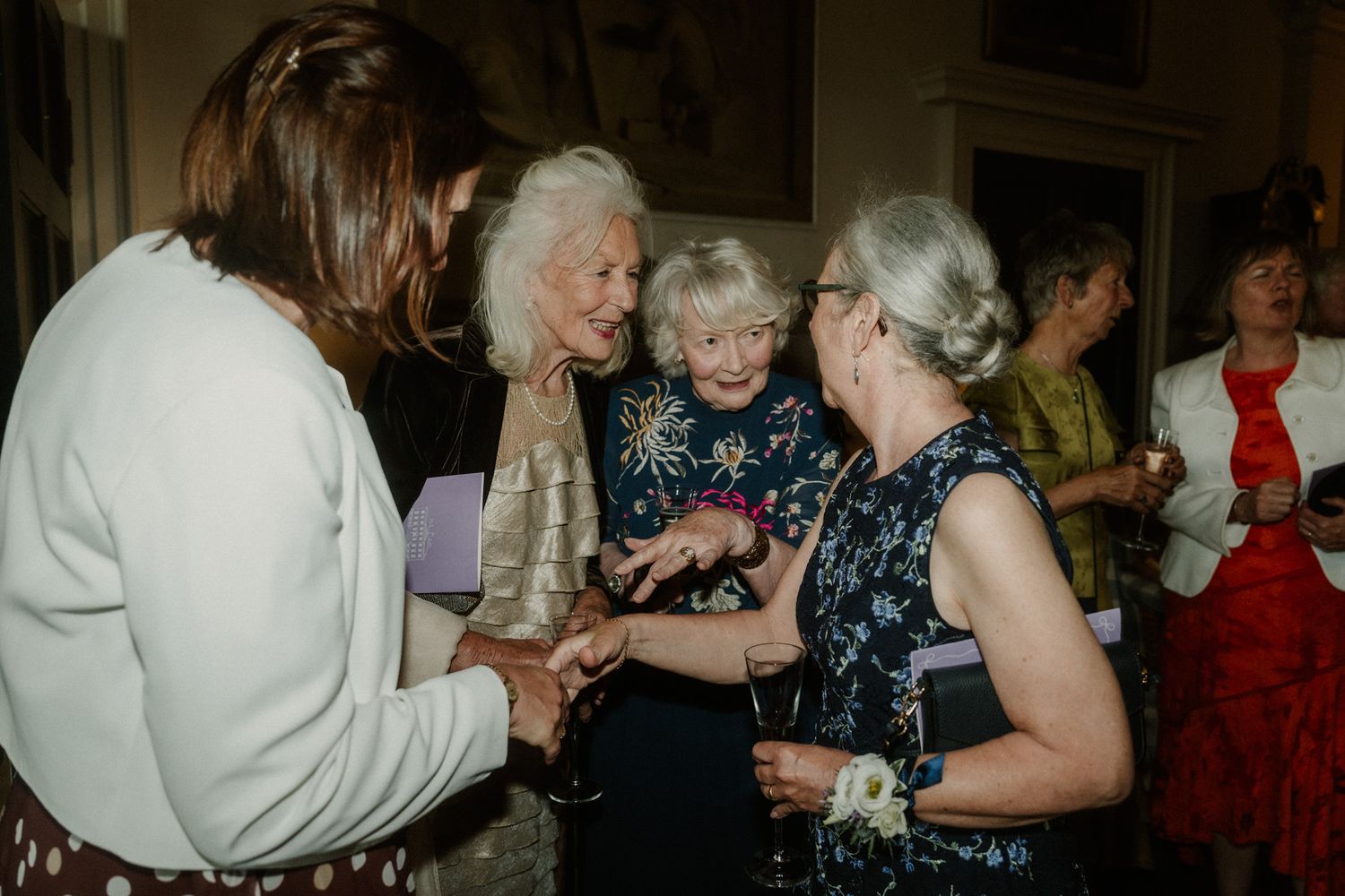 Elderly women socializing at a formal gathering, sharing conversation and laughter at an elegant indoor event.