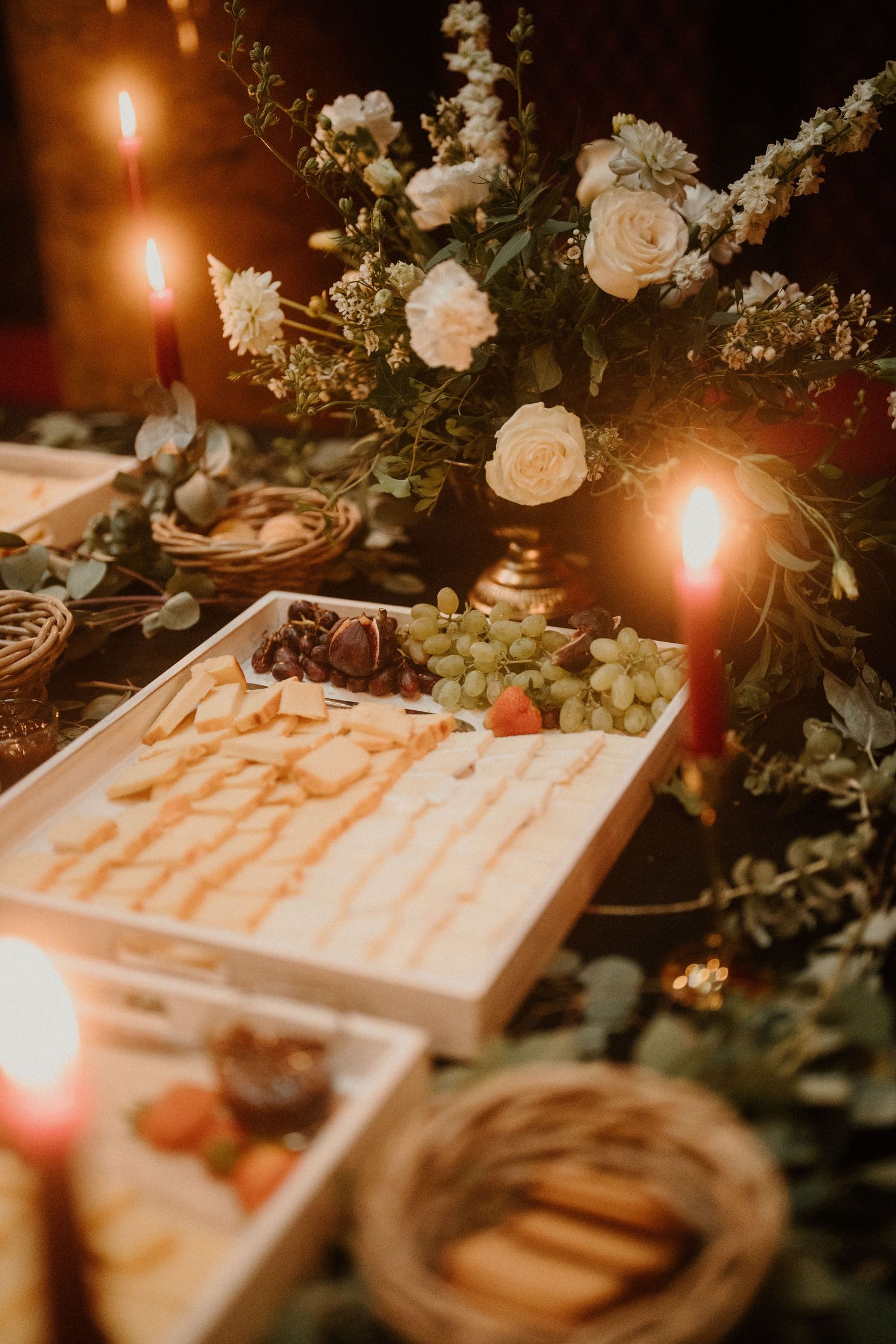Elegant candlelit charcuterie board with grapes, strawberries, crackers, and white roses at a romantic event.